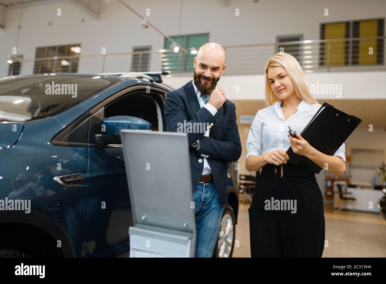 Smiling man and saleswoman in car dealership. Customer and seller in vehicle showroom, male person buying transport, auto dealer business Stock Photo