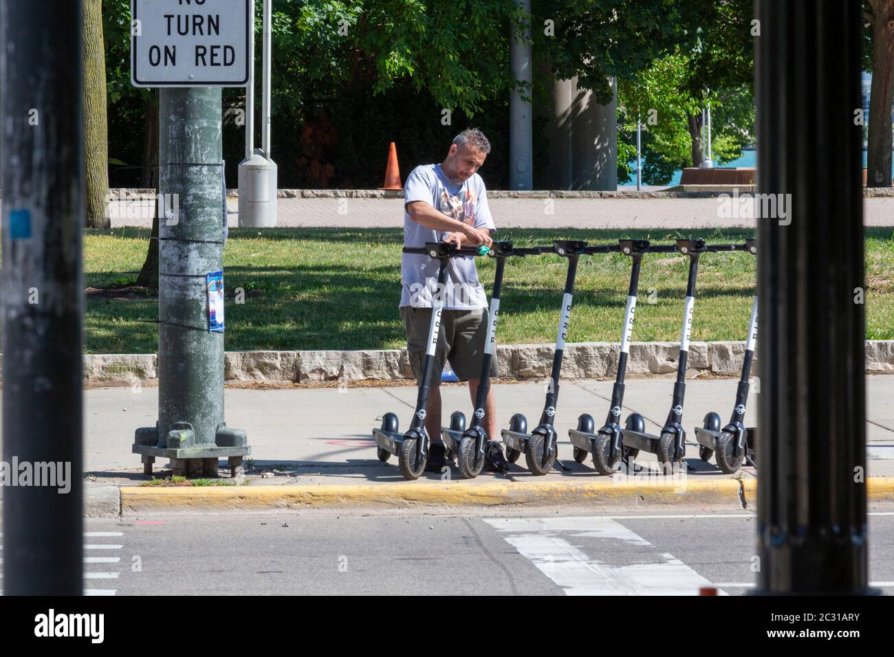 Detroit, Michigan - A worker uses sanitizing wipes to disinfect shared electric scooters parked on a city street during the coronavirus pandemic. Stock Photo