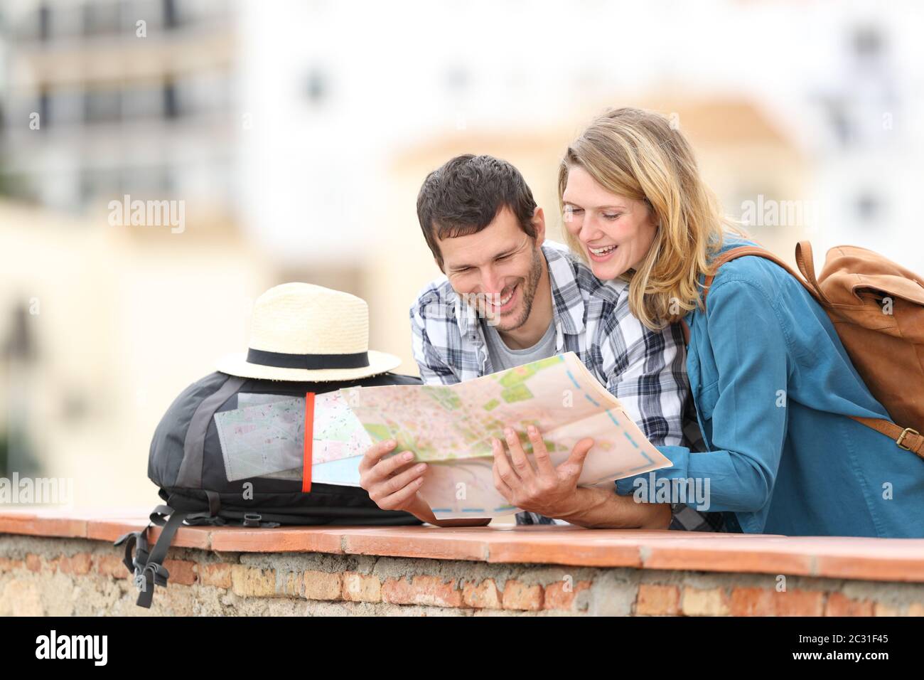 Happy couple of tourists checking map on vacation standing outdoors in a balcony in a rural town Stock Photo