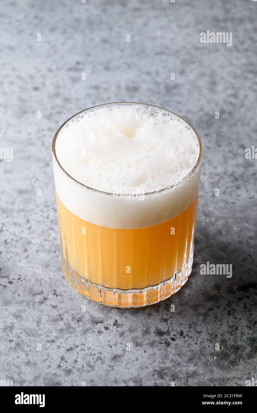 Pisco sour cocktail. Whiskey with lime, egg white, syrup in glass on grey. Vertical shot Stock