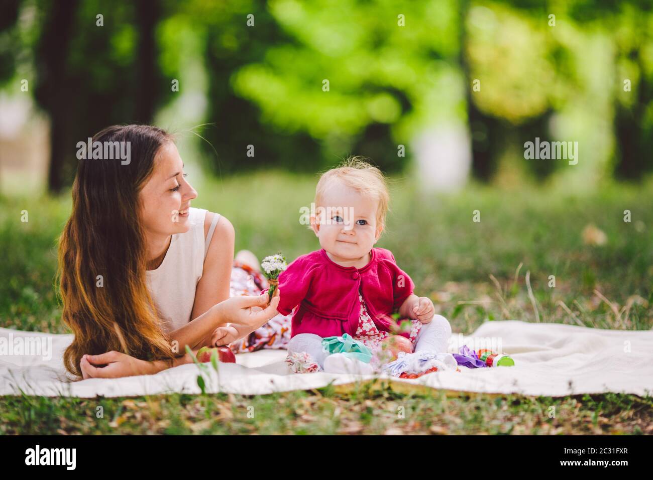 Young pretty mother with daughter lie on a plaid in the park. Family outdoor recreation. Family summer picnic in the park. Mom a Stock Photo