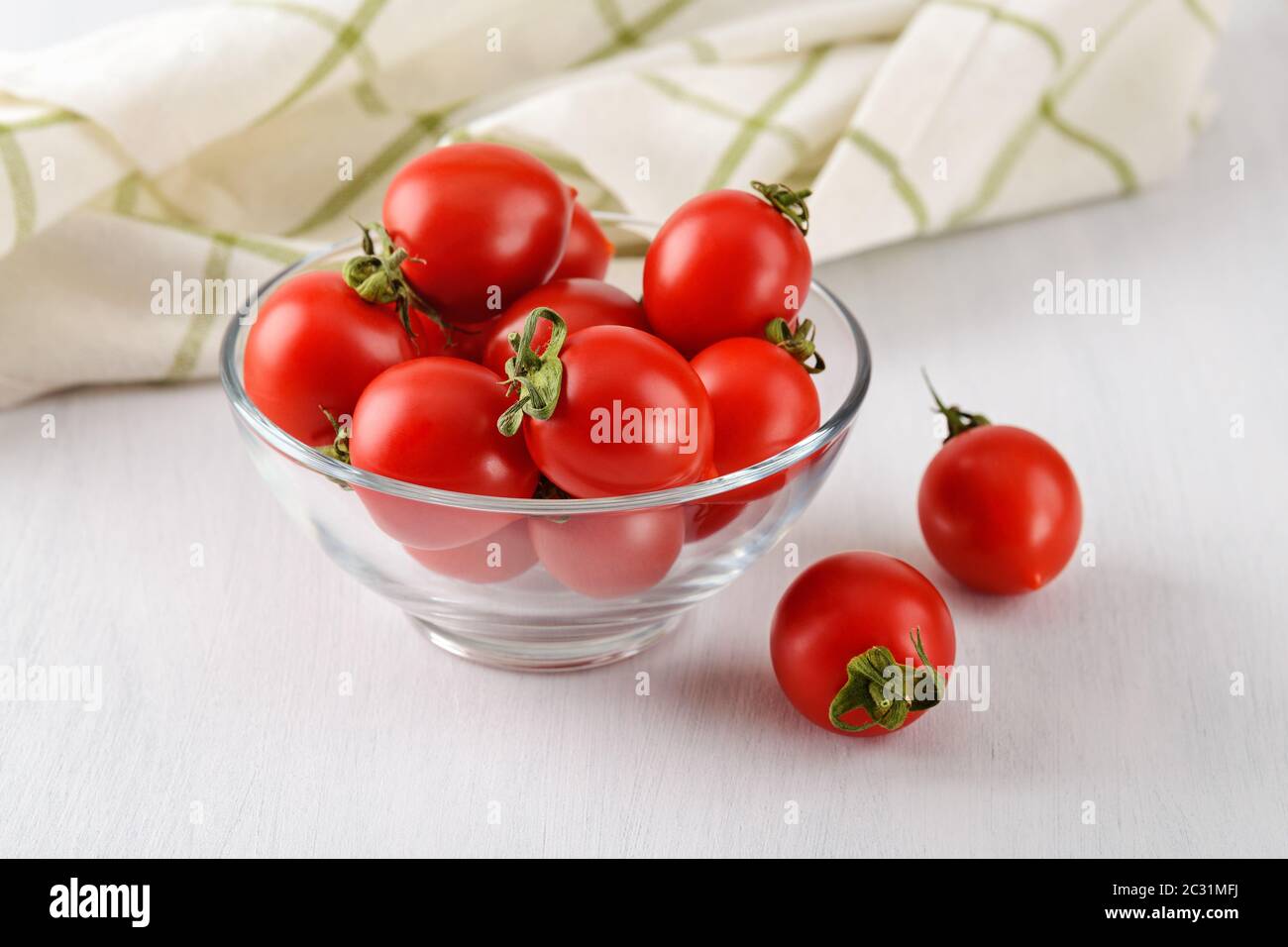 Whole ripe red cherry tomatoes in a glass bowl on a rustic white ...