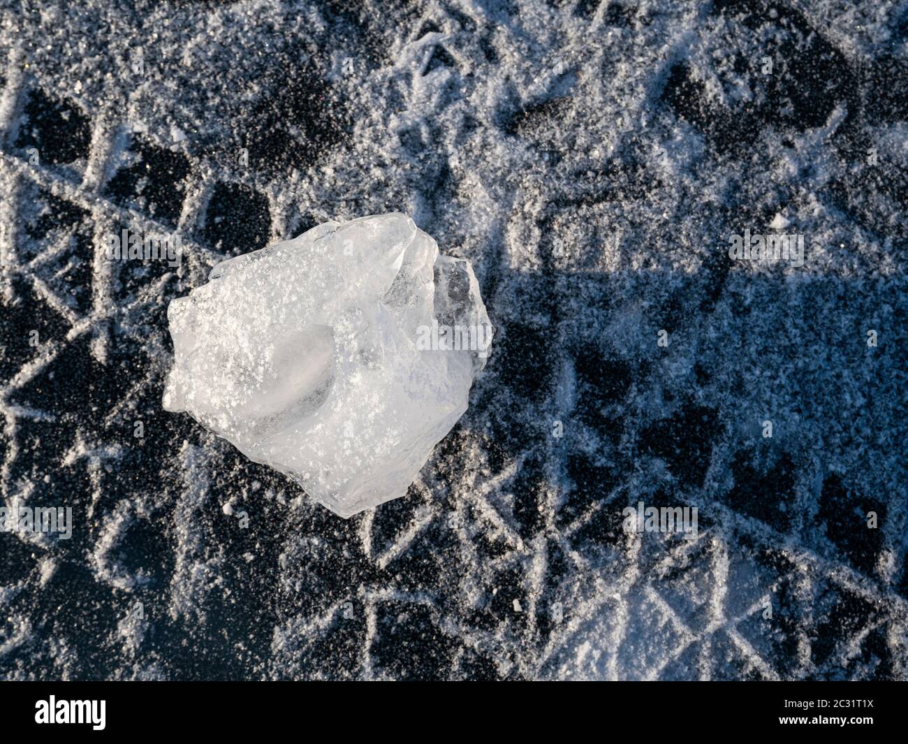 Closeup unusual shapes ice cube on the frozen lake surface. Tire tracks