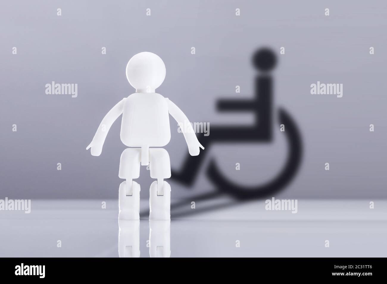 White Human Figure On Reflective Desk Against Grey Background With Shadow Of Disable Icon Stock Photo