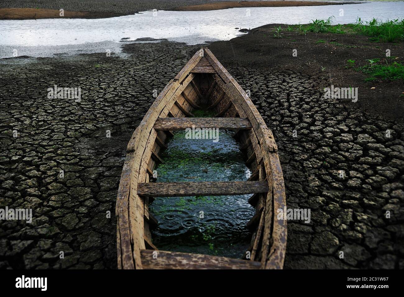 Old canoe on dry lake, river on background, clay cracked soil, mud ground. Climate change, drought, water shortage, environmental disaster. Stock Photo