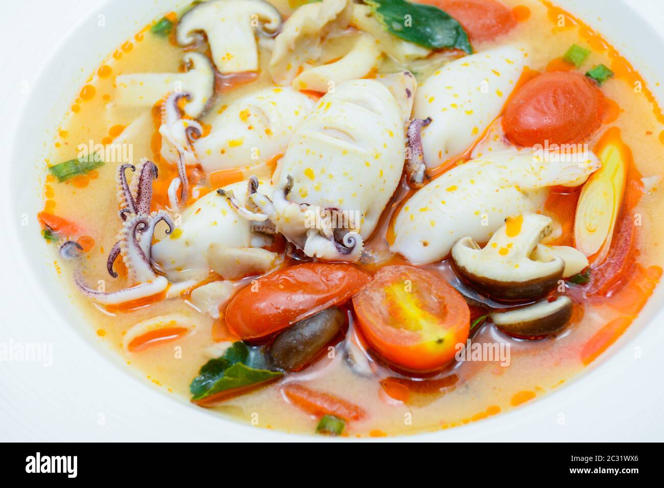 Squids and lemon grass spicy soup with mushrooms, tomatoes and herbs Stock Photo