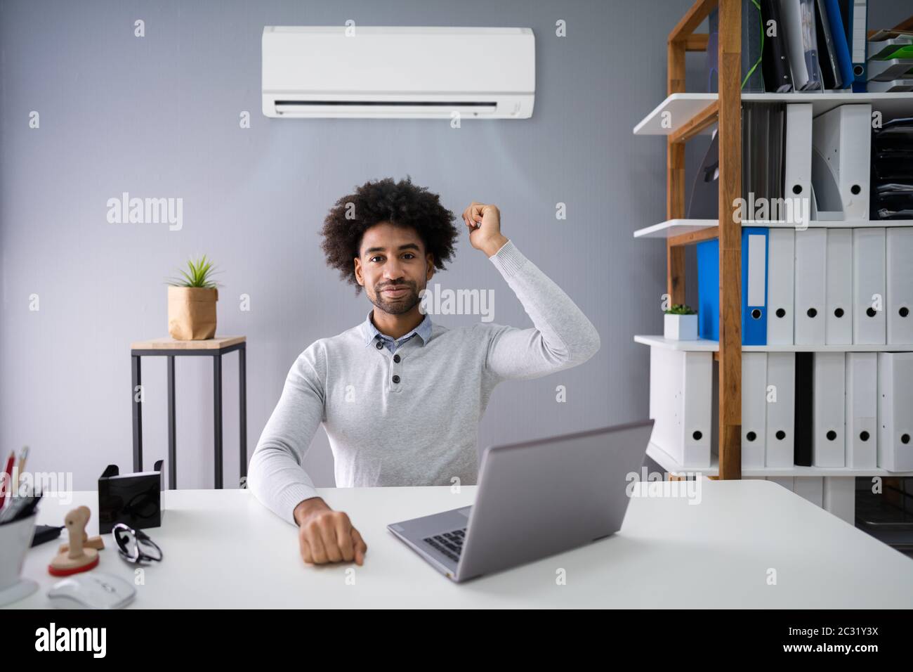 Young Businessman Operating Air Conditioner With Remote Controller In Office Stock Photo