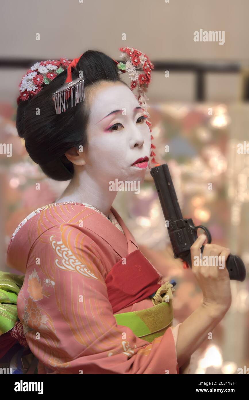 Pretty young Geisha maiko girl in kimono holding a plastic gun in her hand. Stock Photo