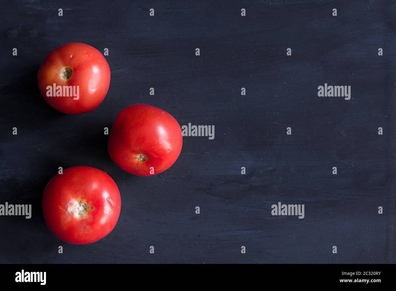 Three tomatoes on a dark blue table. Healthy vegetables Stock Photo