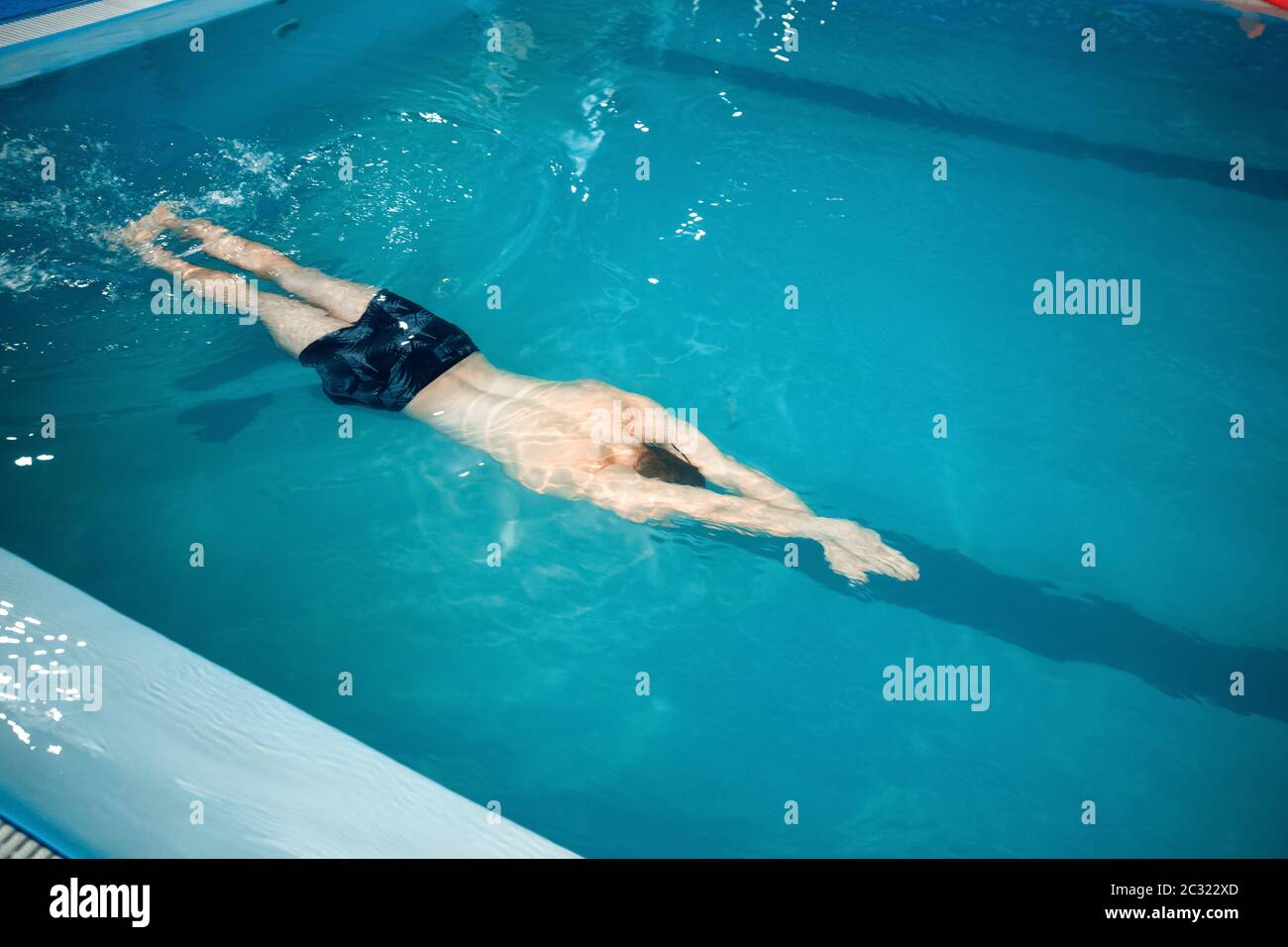 Male swimmer swimming underwater in pool, top view. The man holds his