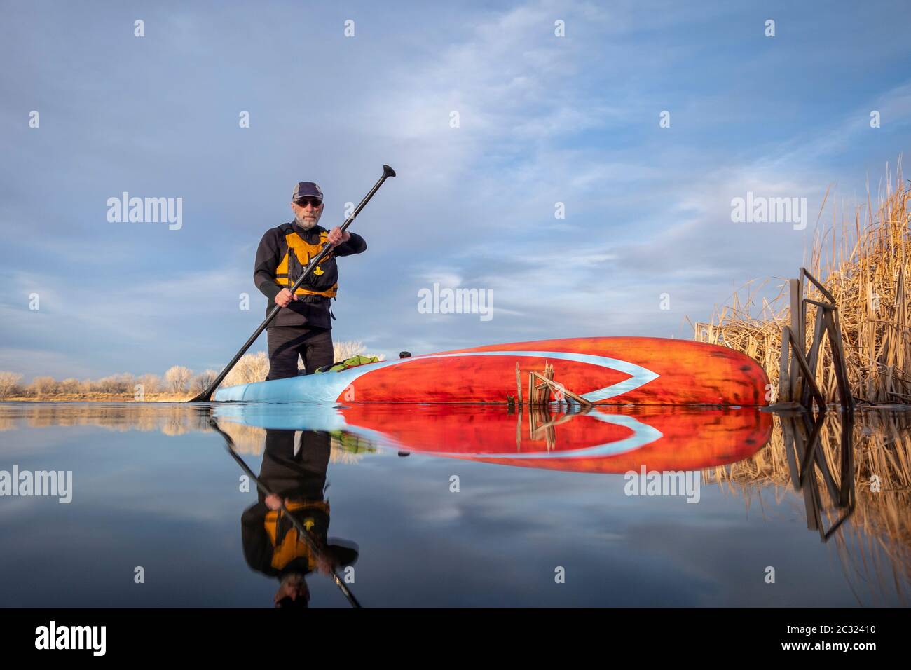 senior male paddler in a wetsuit is paddling a stand up paddleboard on a lake in Colorado