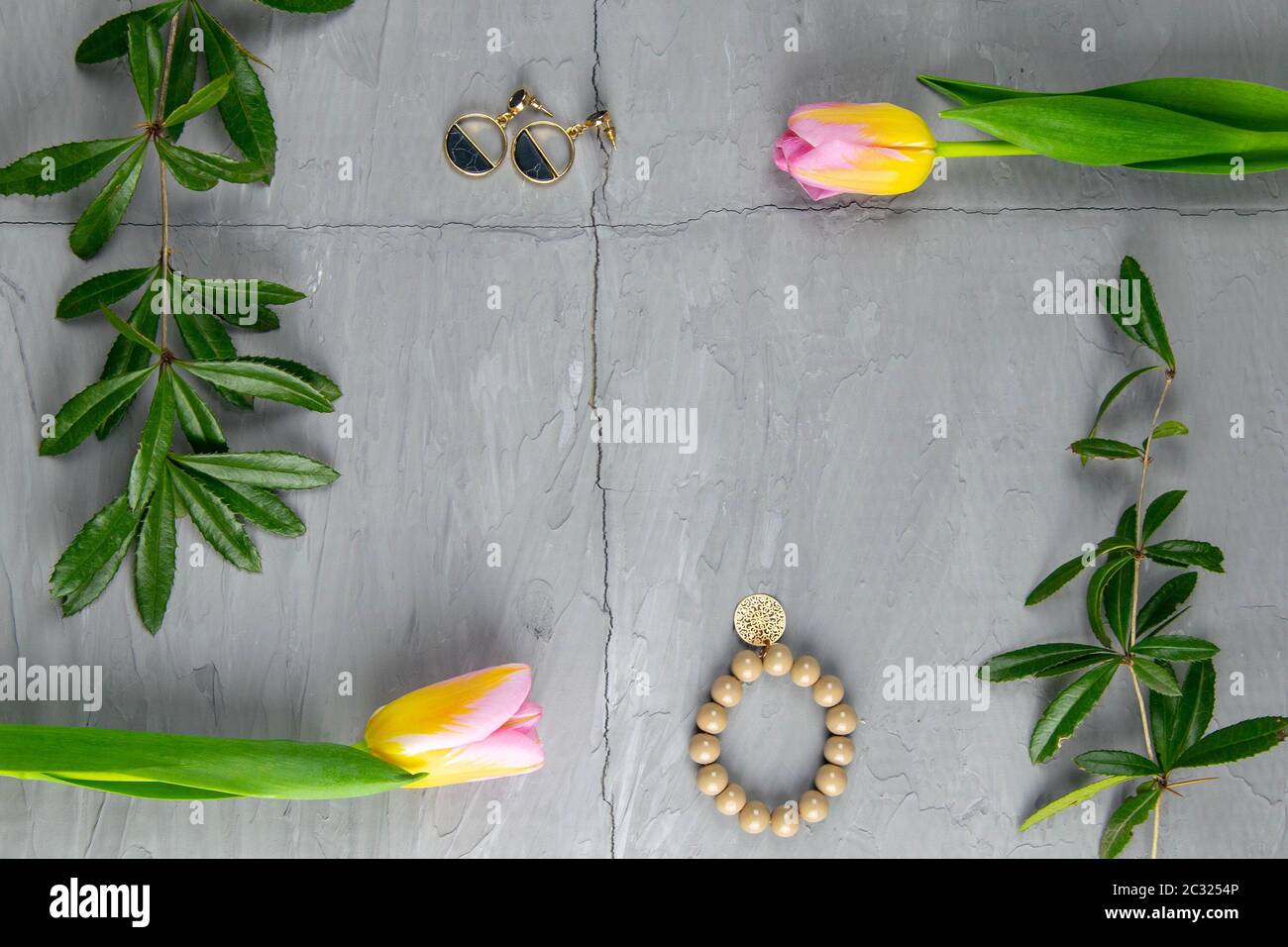 Jewelry, bracelet with keychain and gold earrings together with tulips and green laid on a concrete background. Inside the composition, free space. Stock Photo