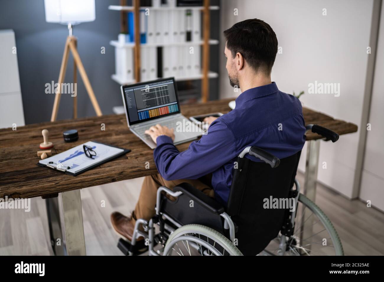 Businessman On Wheelchair While Working On Computer Stock Photo