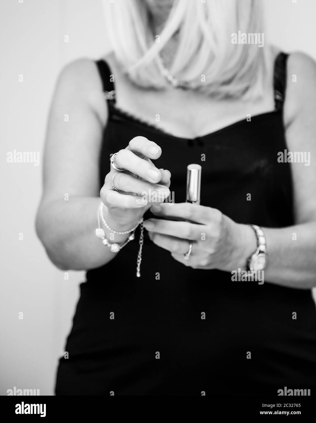A lifestyle monochrome image of a blonde woman putting on a bracelet getting ready to go out for the evening. The image focuses on her hands. Stock Photo