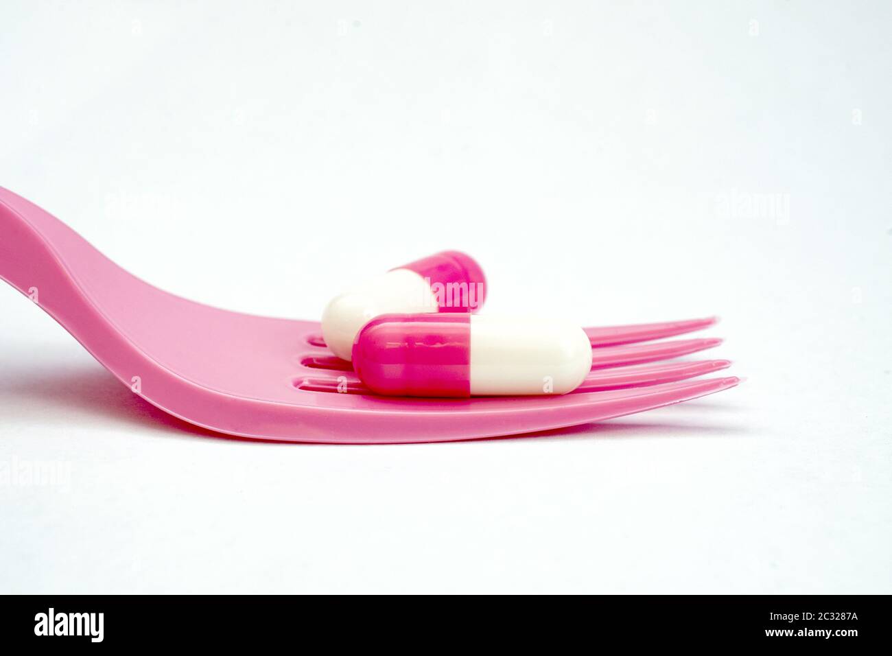 two pink white capsules on a disposable fork on white background Stock Photo