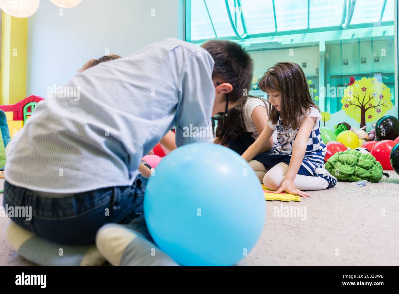 Group of pre-school children surrounding their skilled teacher during an educational activity in the classroom of a modern kindergarten Stock Photo