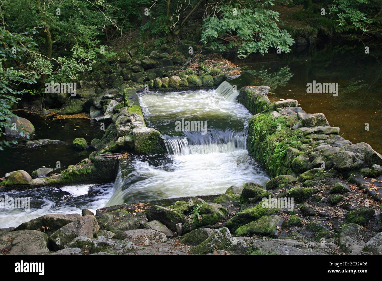 Double weir on a river of two linked pools and water flowing between them. Surrounded by rocks and trees. Stock Photo