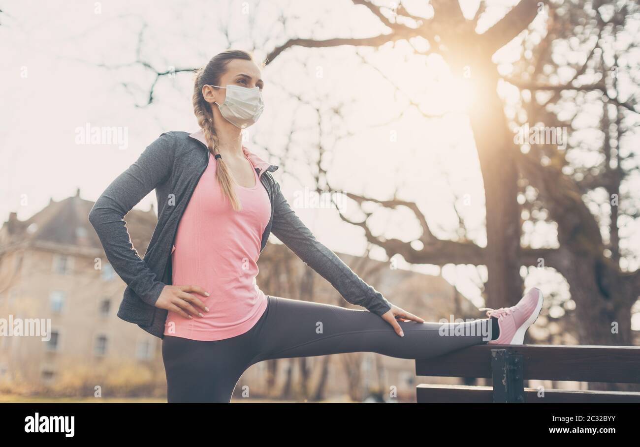 Woman wearing face mask stretching on a park bench outdoors Stock Photo