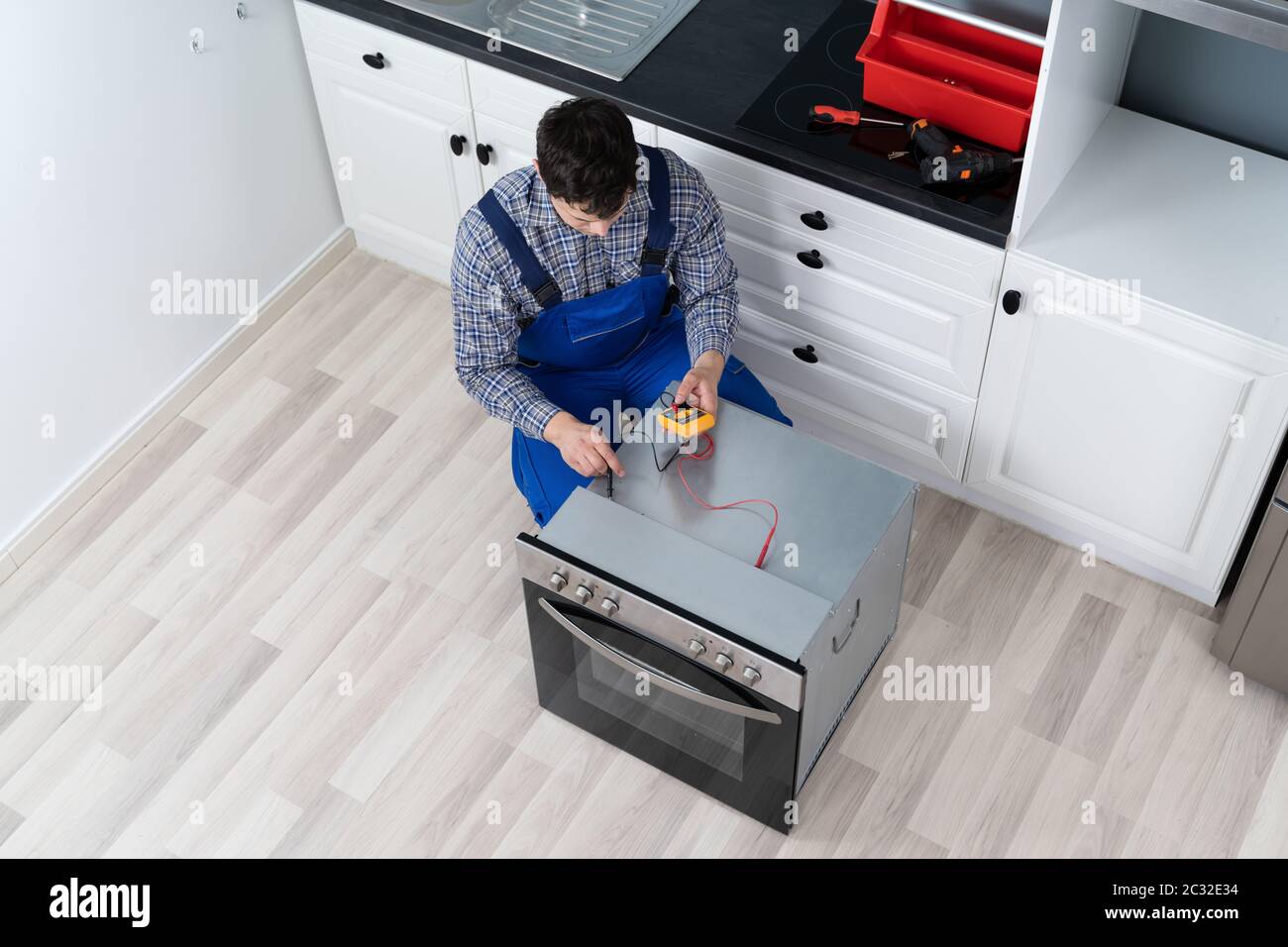 Young Male Technician Checking Oven With Digital Multimeter Stock Photo