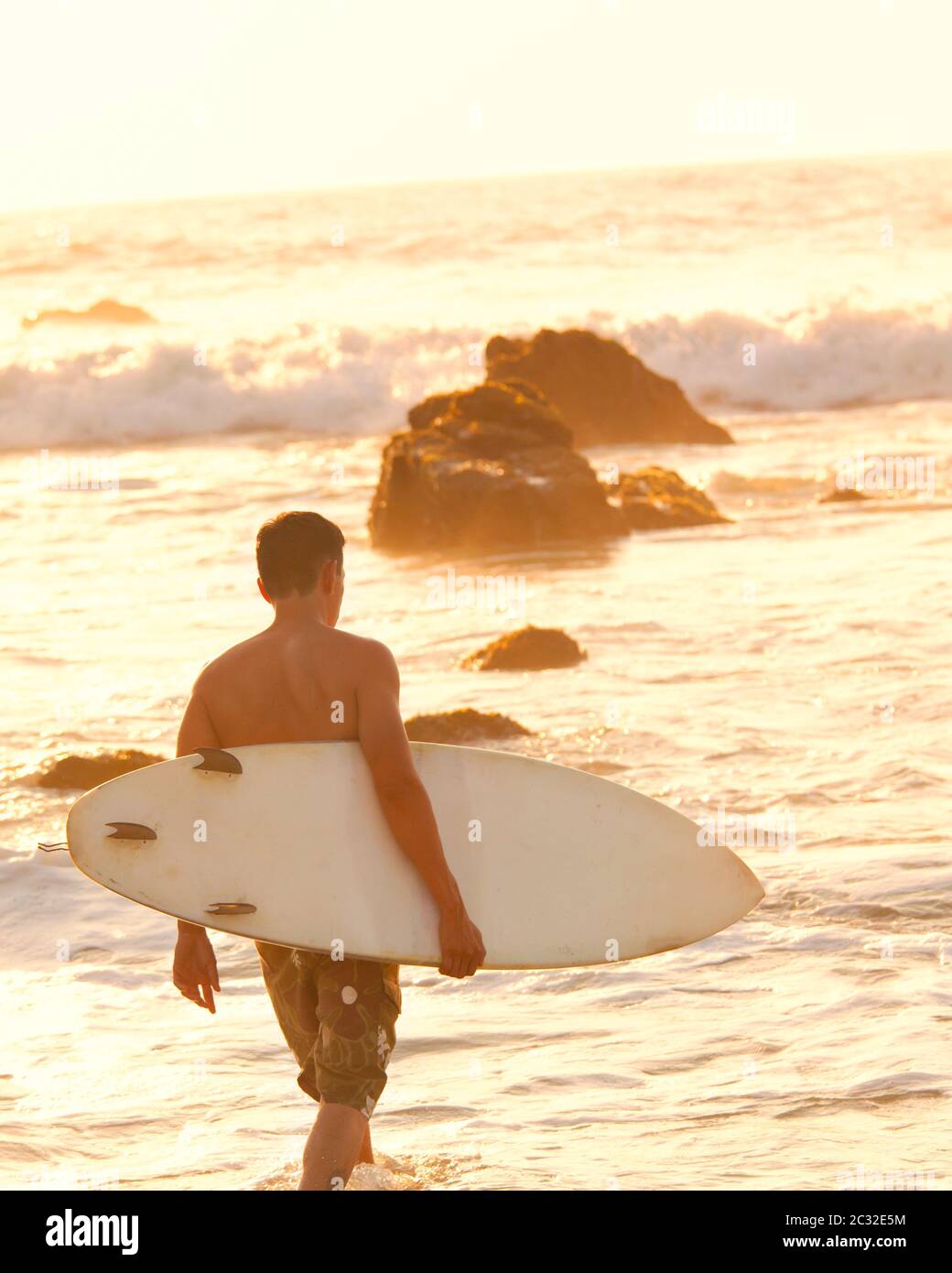 A surfer picks his way through the rocks at La Punta Beach in Puerto Escondido, Oaxaca, Mexico. Stock Photo