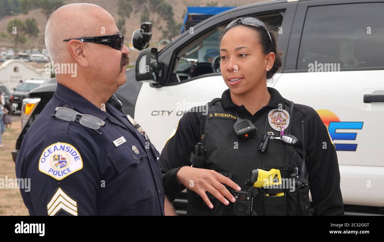 Two police officers, one male, one female, talking with each other in front of a black and white cruiser. Stock Photo