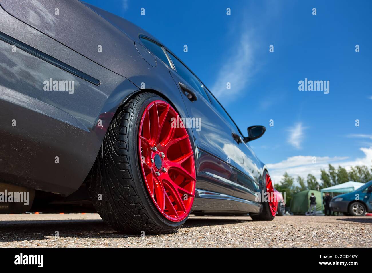 Gray car with lowered suspension and bright red wheels is on the parking. Against blue