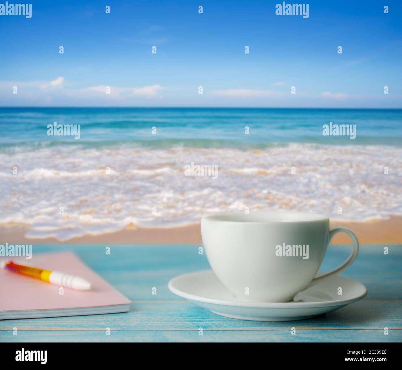 A cup of coffee and notebook with blurred beach sand and blue sky in ...