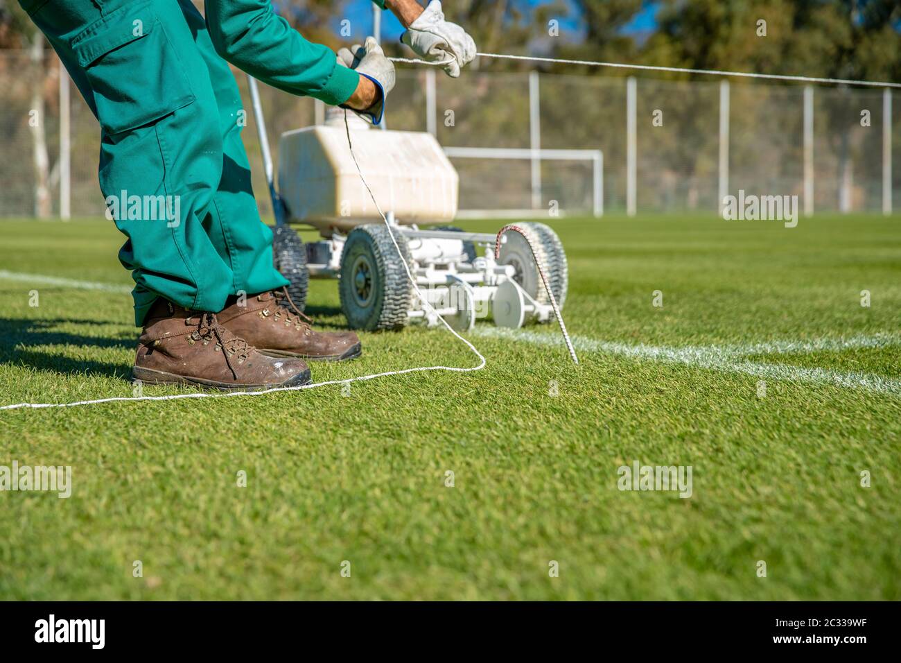 Stretching a rope for lining a football field using white paint on the