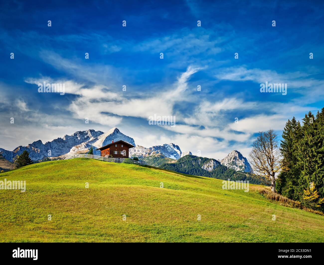Chalet on a meadow at the mountain Eckbauer with alps in background on a sunny day near Garmisch-Partenkirchen, Germany Stock Photo