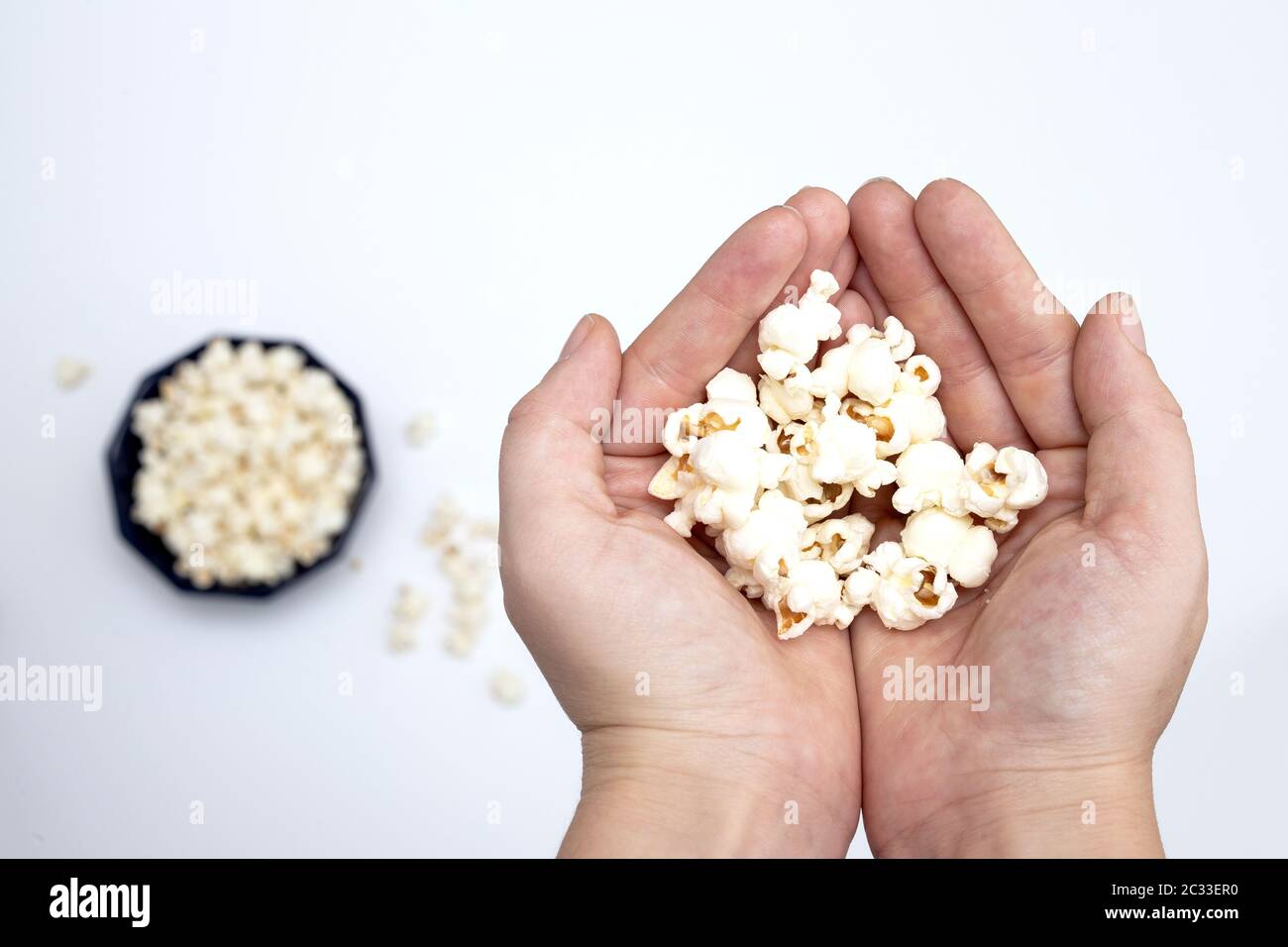 Person holding popcorn in hand top view, with popcorn in bowl isolated on white background close-up Stock Photo