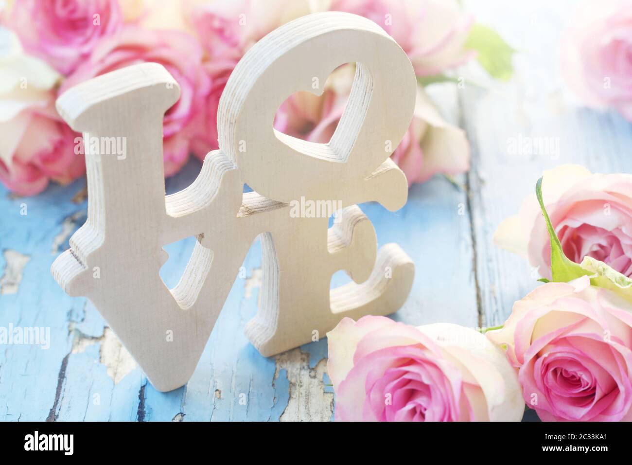 The Word 'Love' In Wood With Pink Roses On A Blue Background Stock Photo