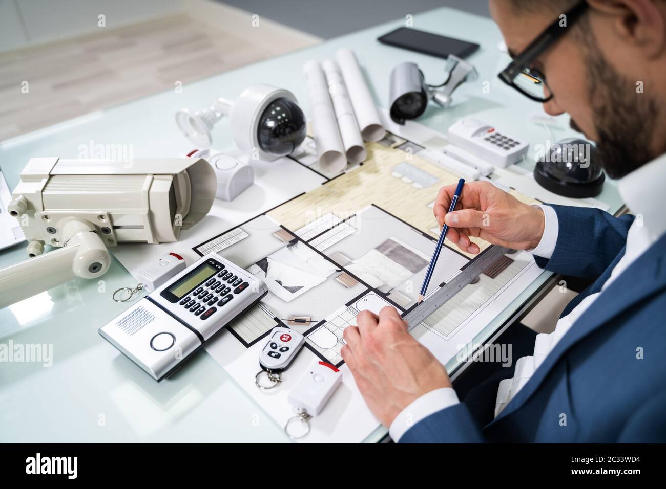 Architect Drawing Blueprint With Various Security Equipment On Desk Stock Photo