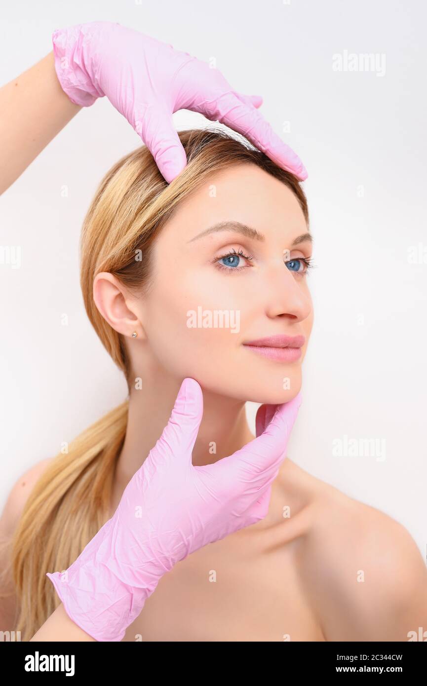 Closeup of beautician hands in gloves touching young woman's face