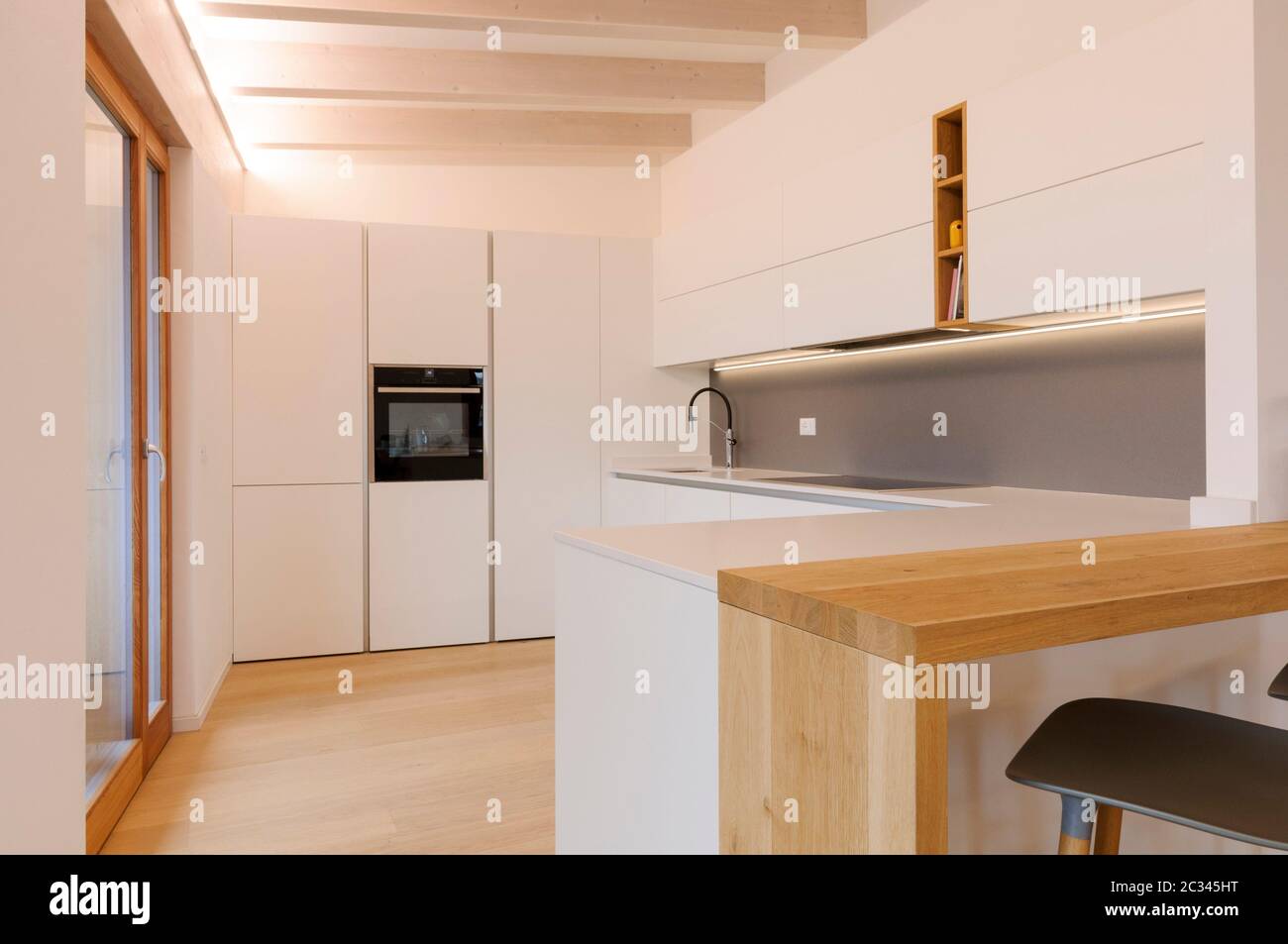 Modern and elegant kitchen interior with white cabinets, induction hob and wooden inserts. Contemporary Scandinavian style Stock Photo