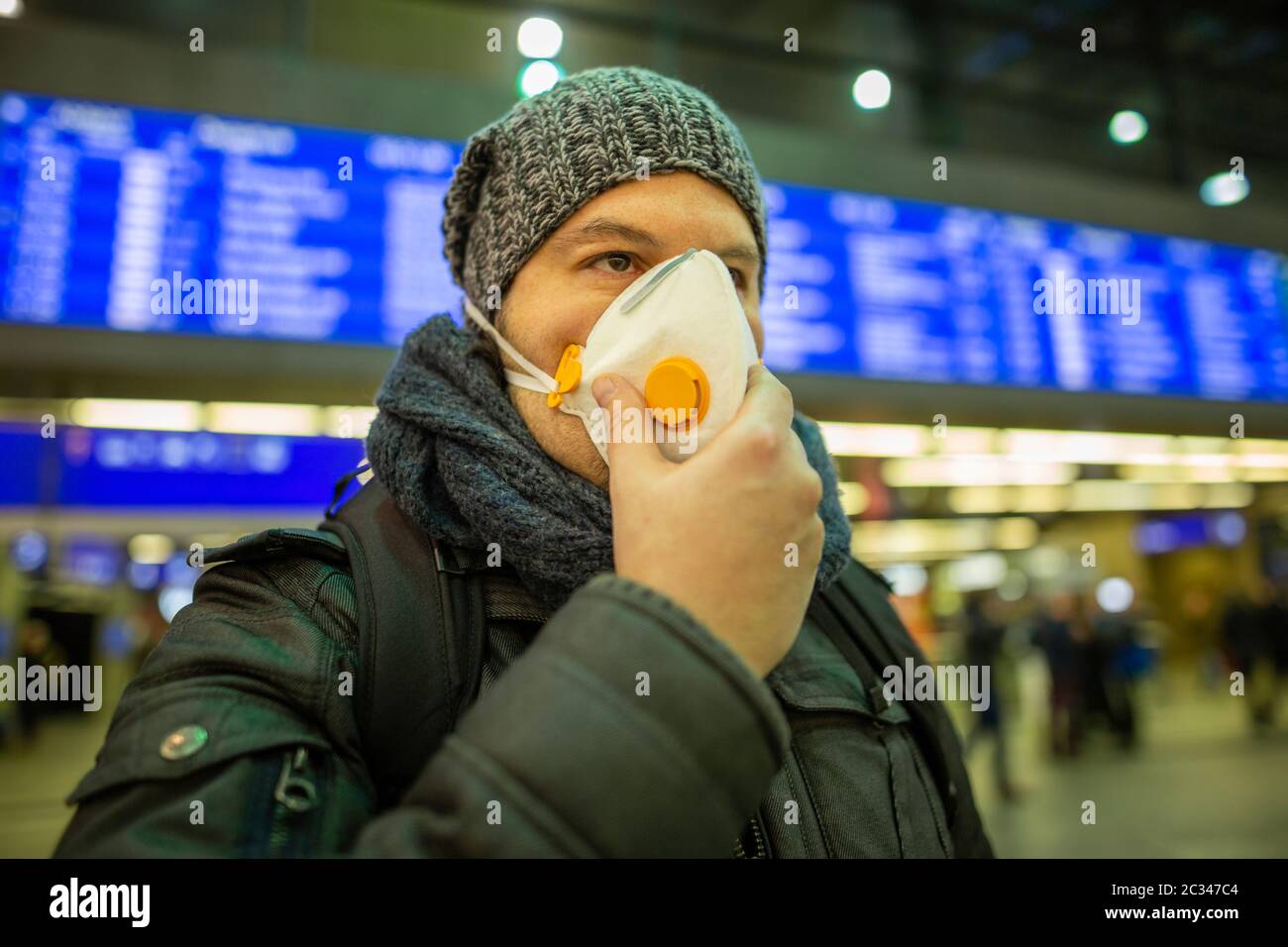 Man wearing a respirator mask device for health protection at an airport or railway train station in Stock Photo