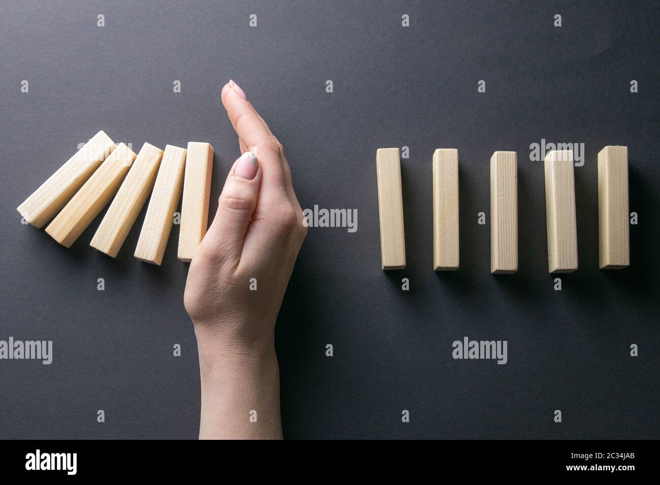 Top view whomen hand stopping falling dominos in a business crisis management conceptual image. Stock Photo