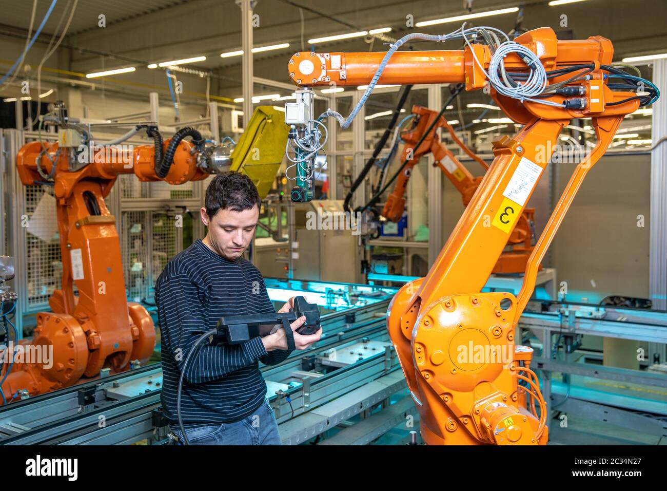 production engineer programs the robotic arms on the production line in a factory. Stock Photo