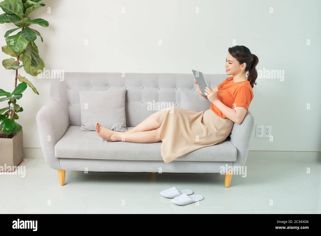 Beautiful young woman using tablet sitting on sofa at home at living room. Stock Photo