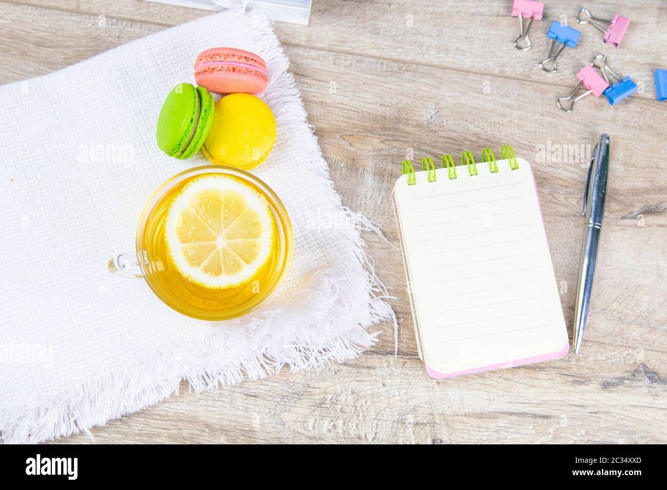 An open notebook with a silver pen, a cup of mint tea with lemon and multi-colored muffins stand next to it. Stock Photo