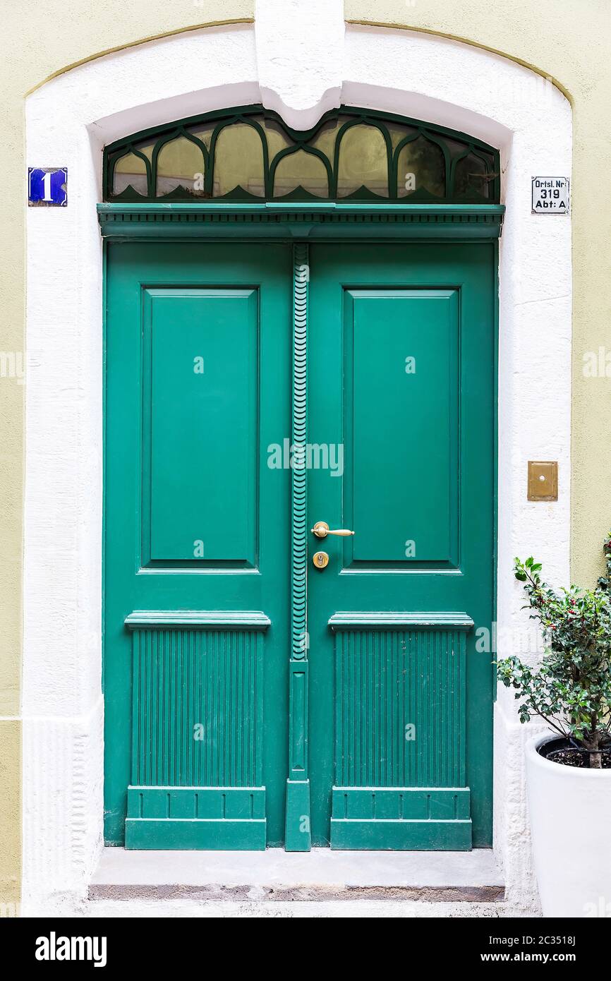 Old green double-leaf front door with a stone door frame and historical house number Stock Photo