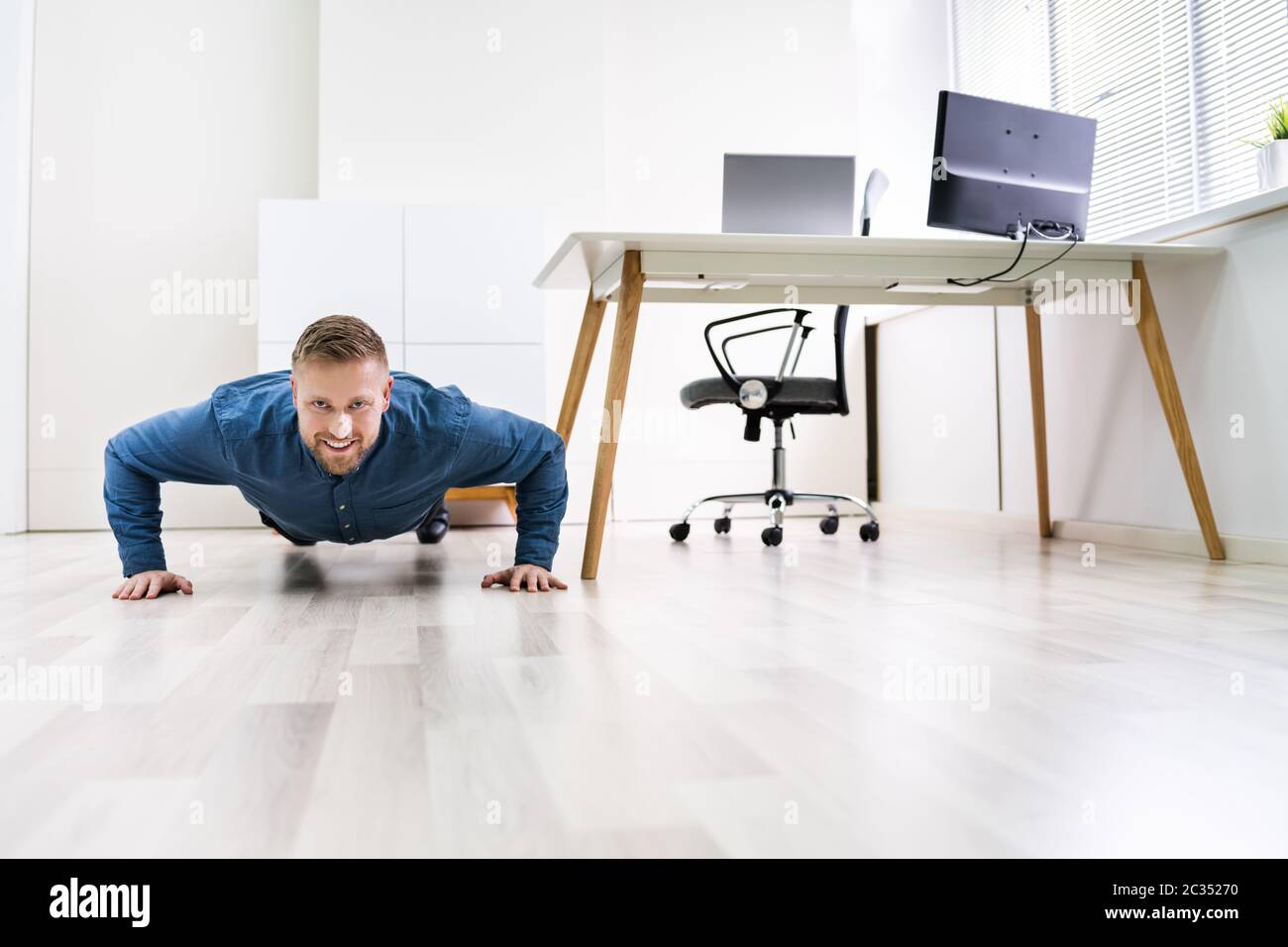 Businessman Doing Push Up On Hardwood Floor In Office Stock Photo