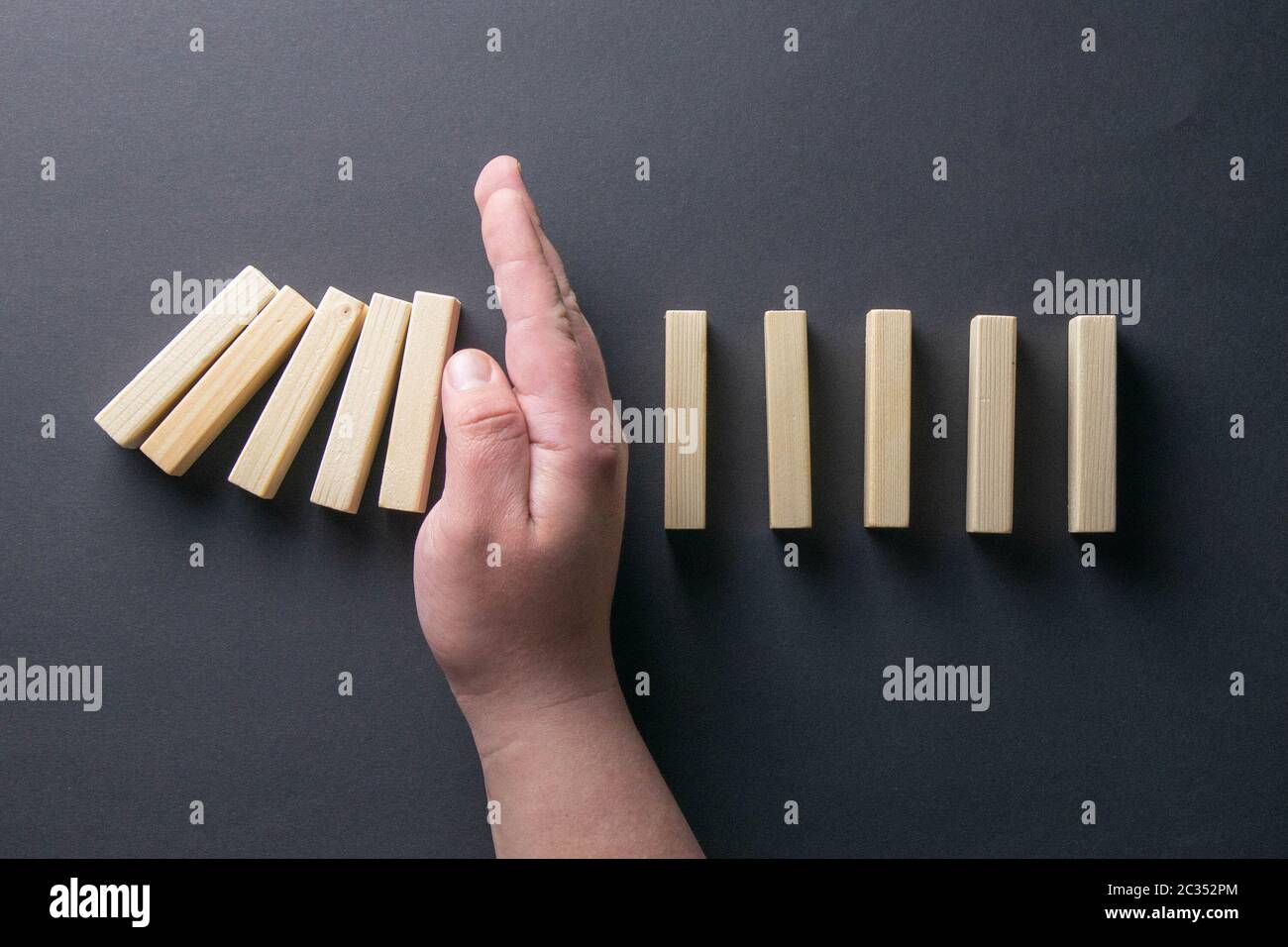 Top view man hand stopping falling dominos in a business crisis management conceptual image. Stock Photo