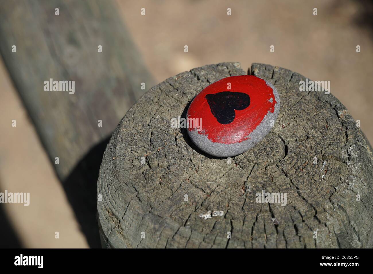 One small flat rock painted red, with a black heart, commemorating the BLM or Black Lives Matter movement. Was placed on a wooden fence post, sunlit. Stock Photo