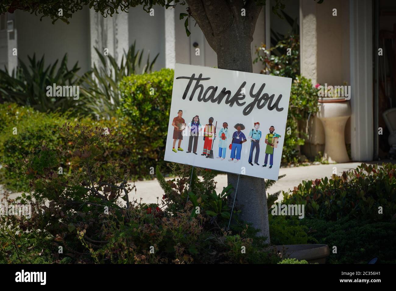 A colorful poster under a neighborhood tree thanking the many essential workers (depicted)for their efforts during the corona virus pandemic.Gratitude Stock Photo