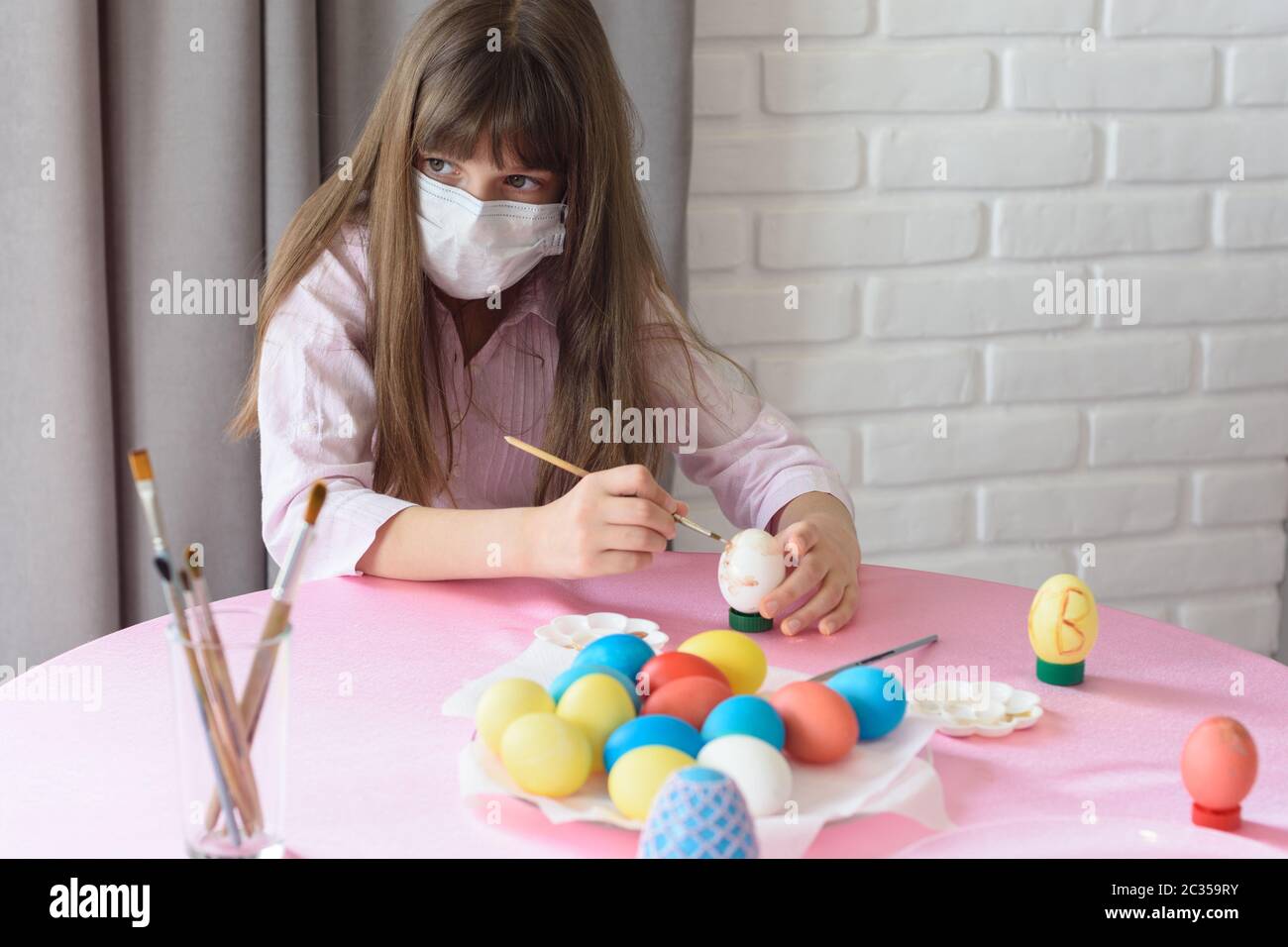 Sad sick quarantined girl paints Easter eggs Stock Photo