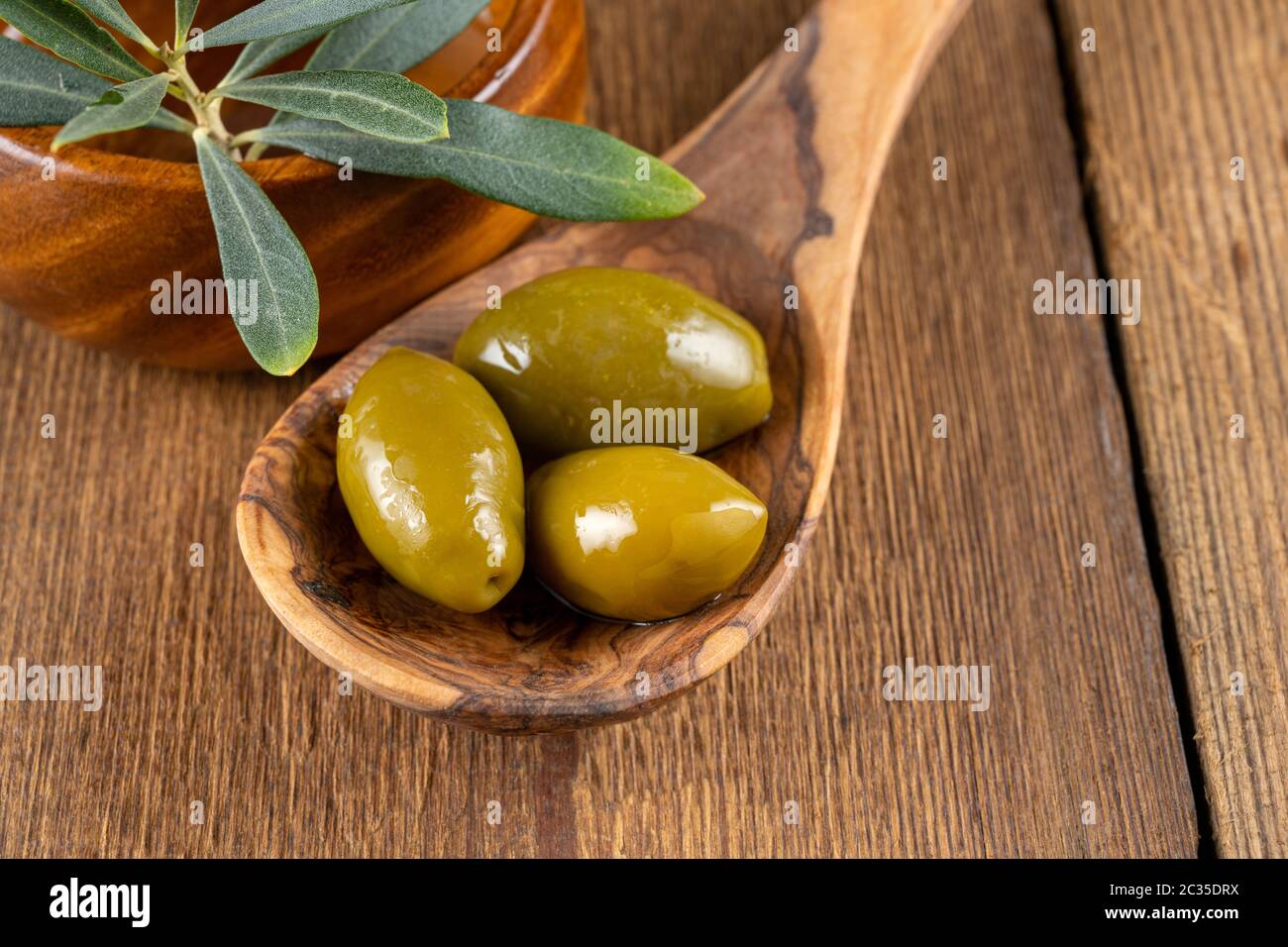 Green olives on a wooden cooking spoon and an olive branch in a wooden ...