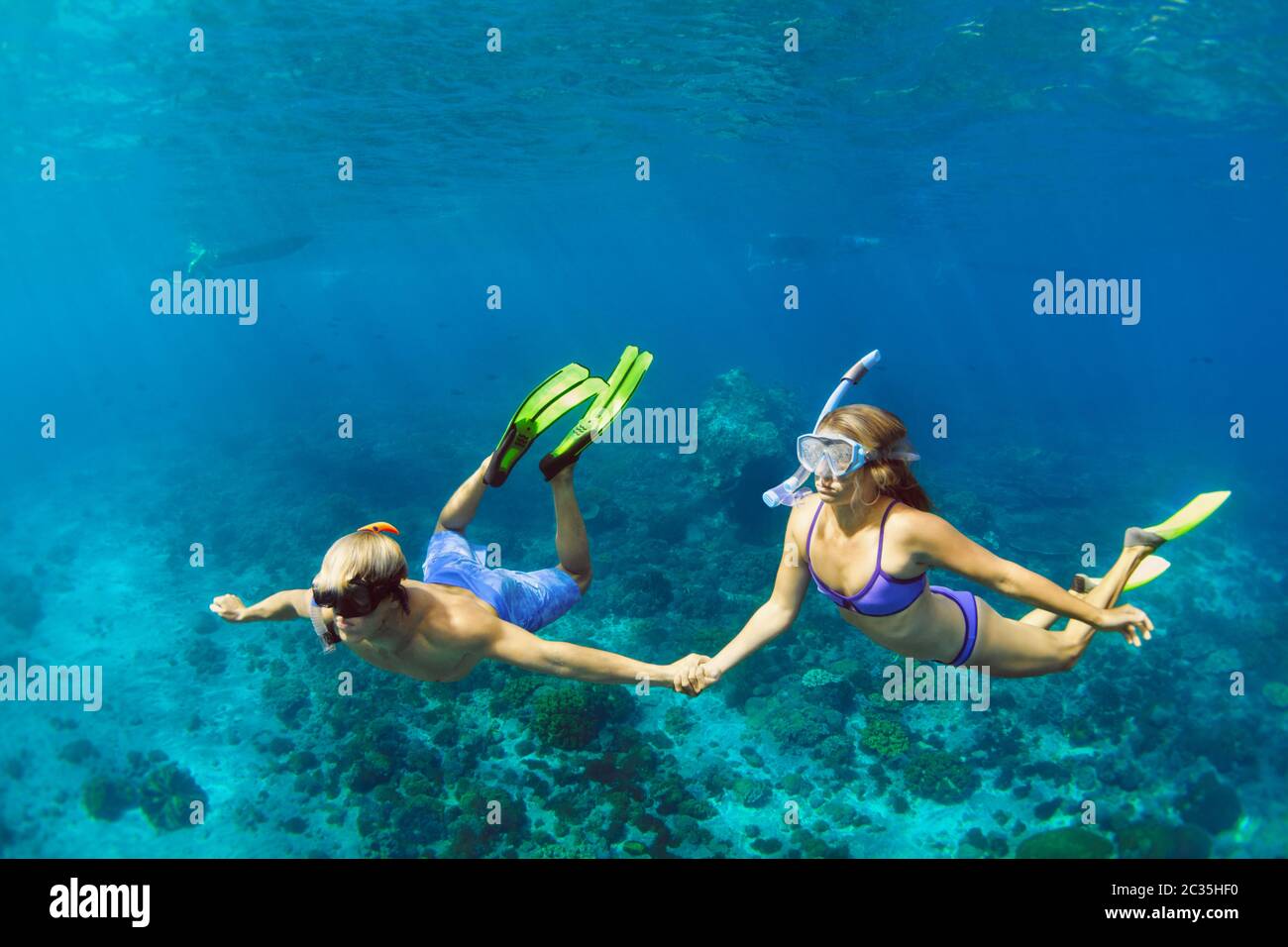 Happy family vacation. Young couple in snorkeling mask hold hand, free dive underwater with fishes in coral reef sea pool. Travel lifestyle Stock Photo