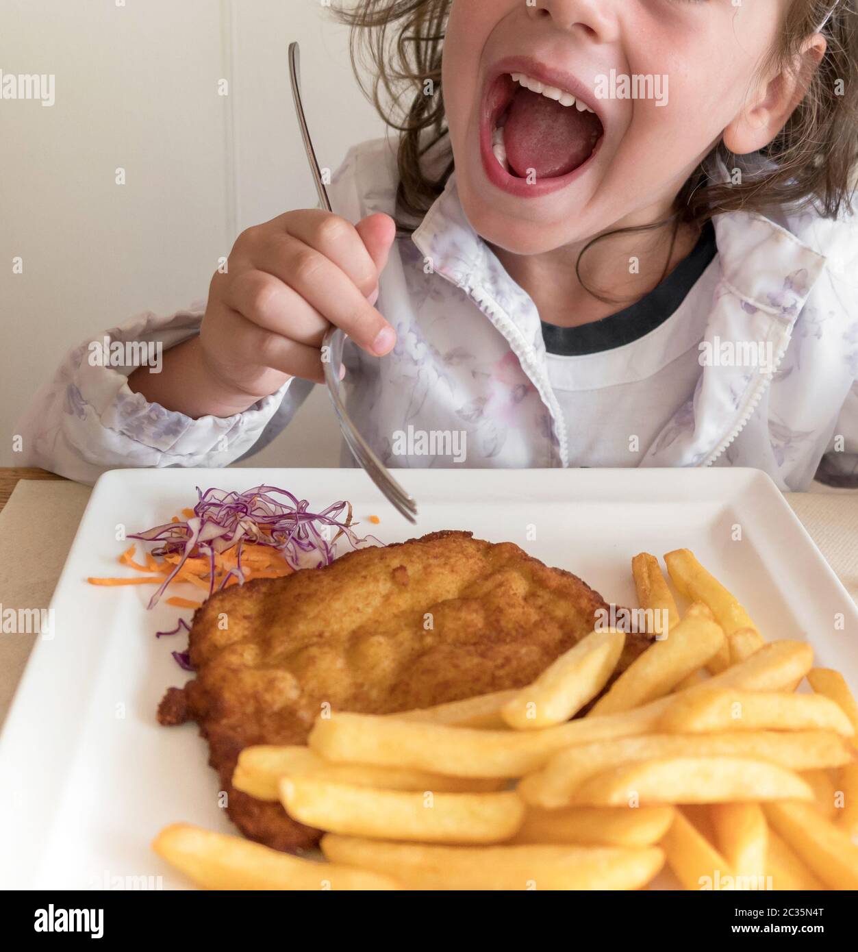 Little Italian girl eating breaded meat and french fries Stock Photo
