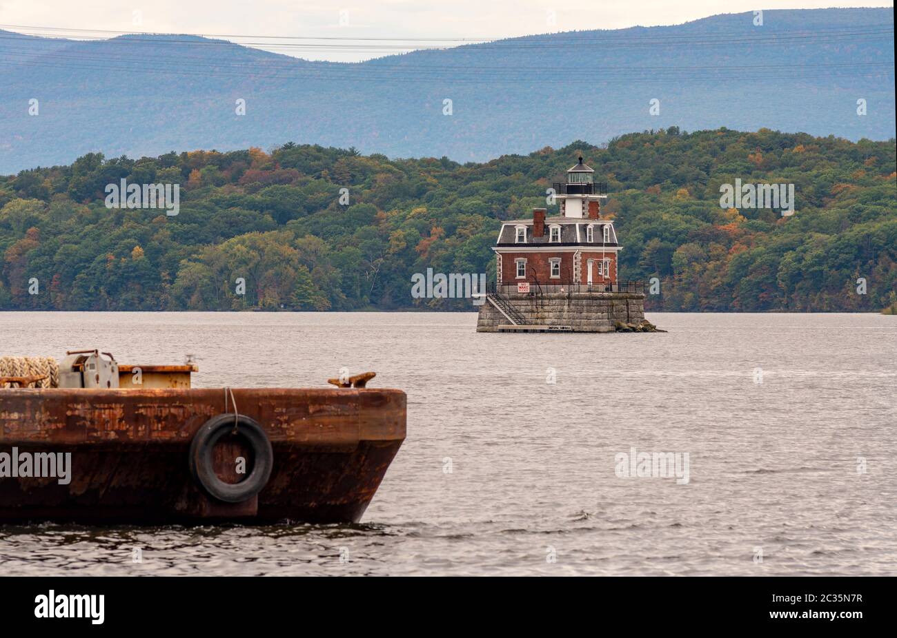 A rusty old barge sits in the foreground near the Hudson Athens Lighthouse in Upstate New York USA Stock Photo