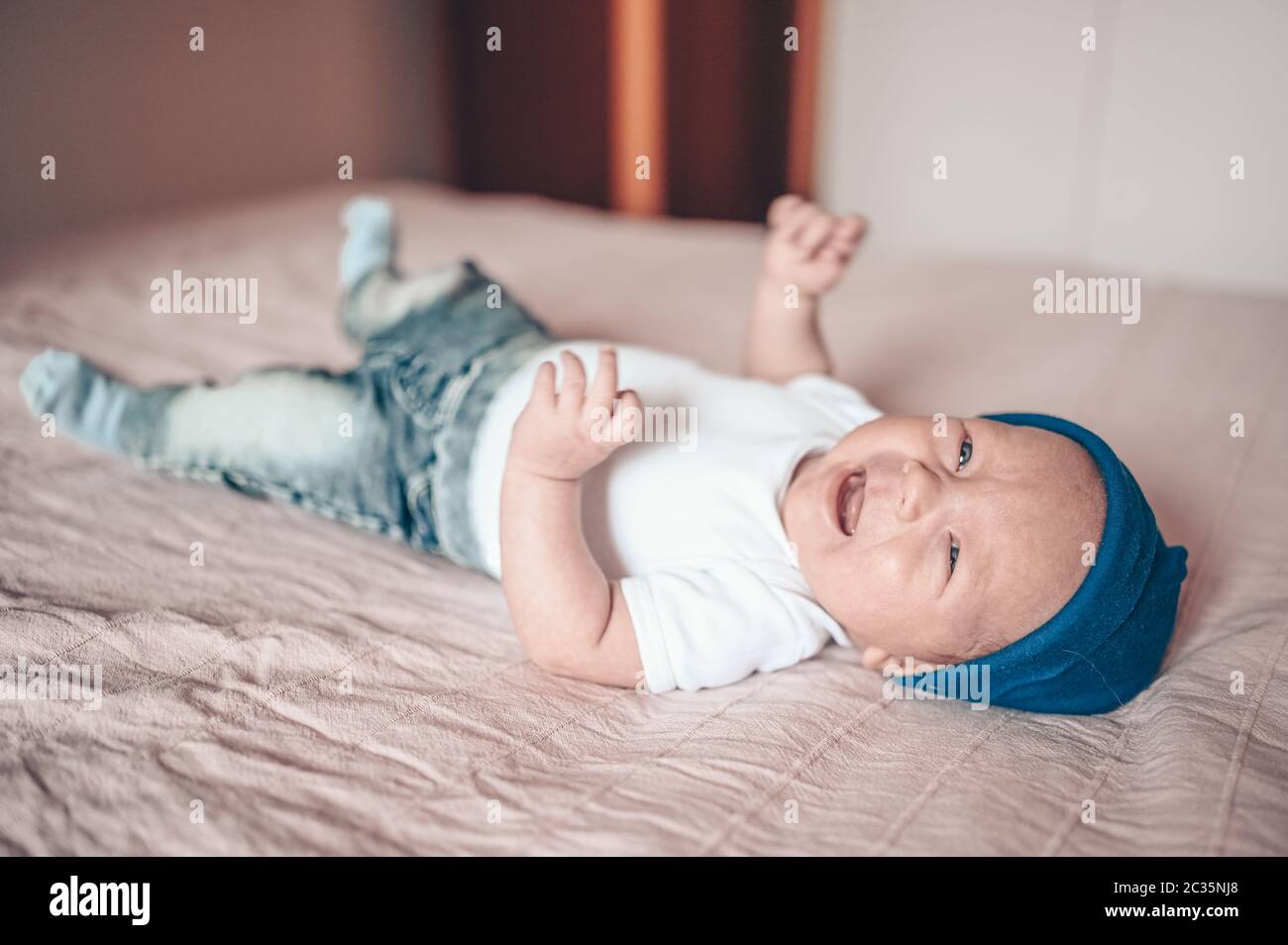 Cute crying little baby boy lying on pink blanket at bedroom. Newborn